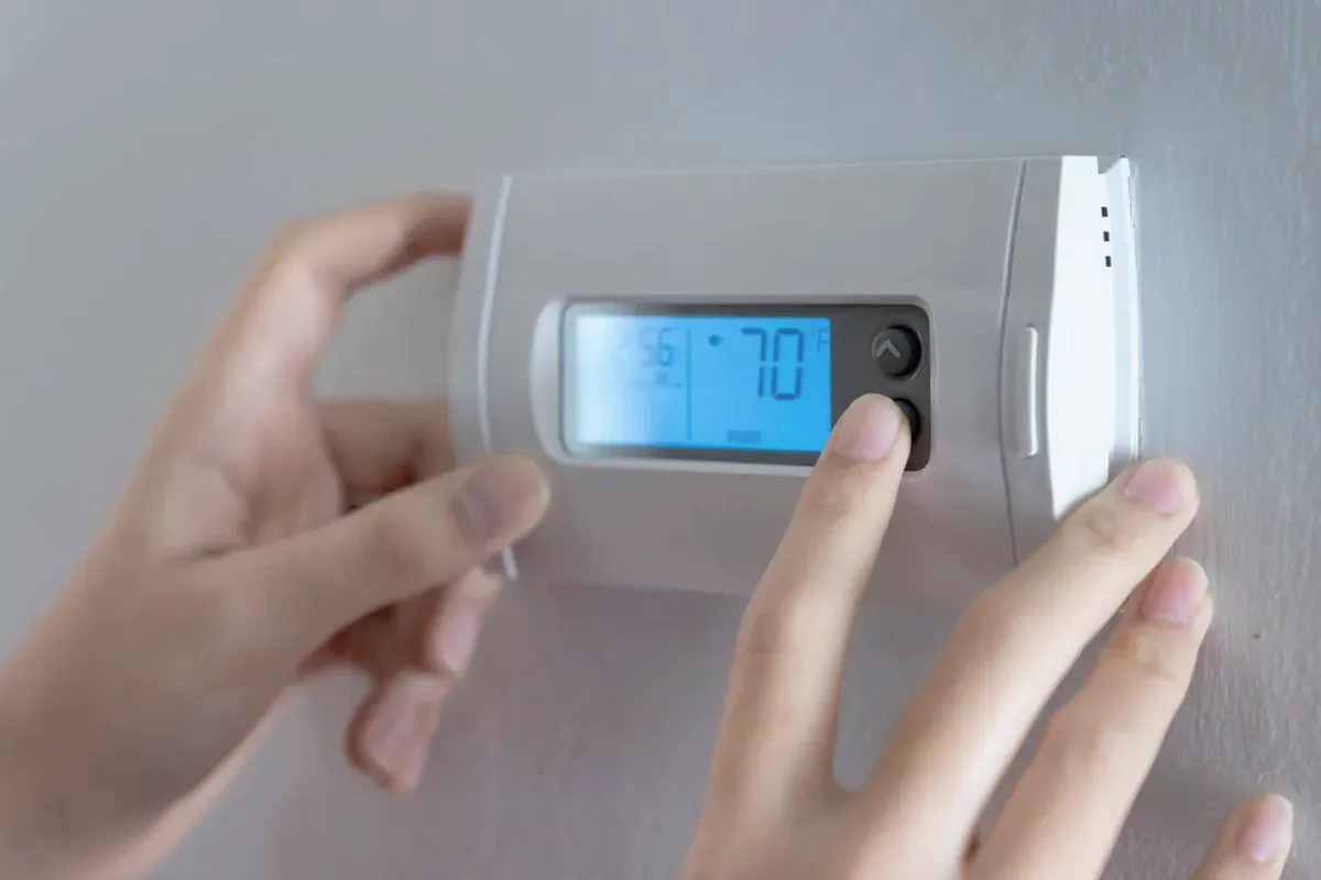 Hands adjusting a digital wall thermostat